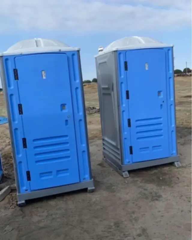 Two blue standard porta potties with gray bases standing on a dirt job site, ready for a construction crew